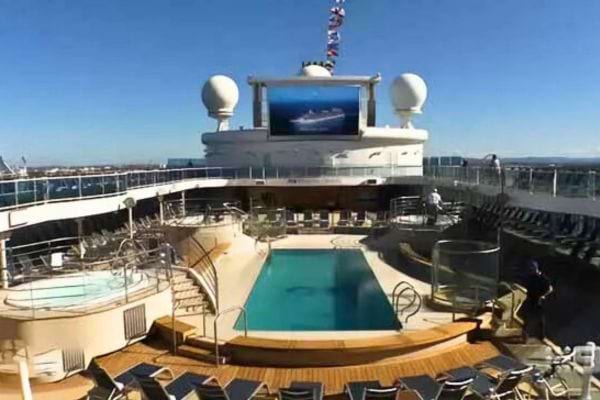 Piscine et chaises longues sur le pont d'un navire de croisi&egrave;re sous un ciel bleu.