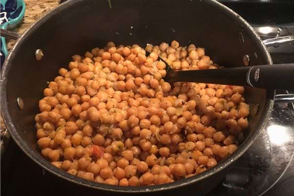 Une poêle sur le feu avec des pois chiches cuits, des peaux partiellement retirées.
