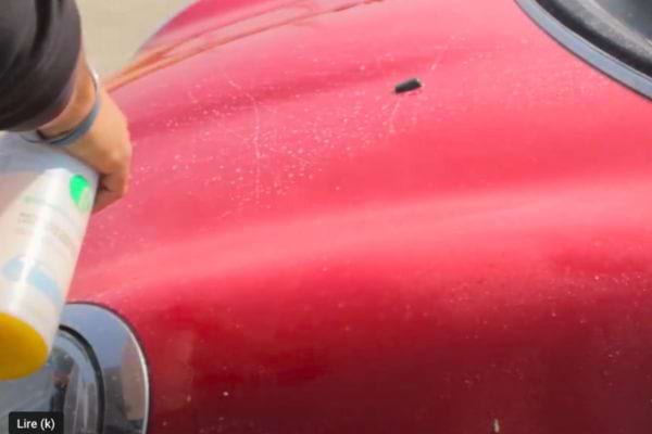 Application d'un produit nettoyant en aérosol sur la surface supérieure d'une voiture rouge.