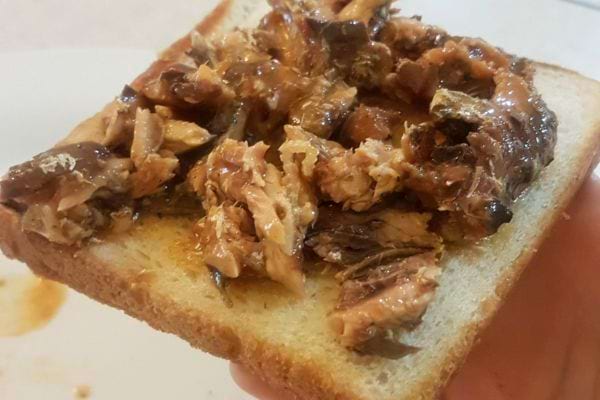 Sardines en morceaux émiettées sur une tranche de pain.