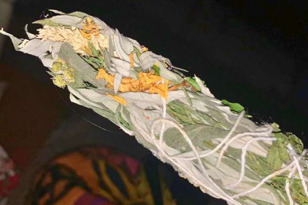 Un bâton de sauge blanche enroulé de fils blancs, parsemé de pétales jaunes, pour la fumigation.