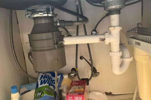 Espace sous évier avec tuyaux et produits de nettoyage.