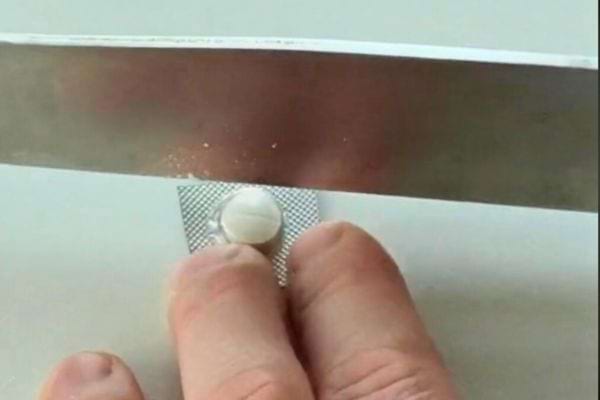 Un comprimé avec une ligne tracée sur le dessus est placé entre deux doigts, prêt à être coupé.