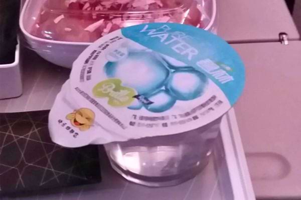 Un petit verre d'eau avec un couvercle en plastique sur une tablette d'avion.