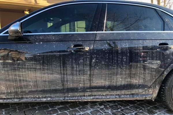 Portière d'une voiture noire couverte de saleté et de traces de lavage sans eau.