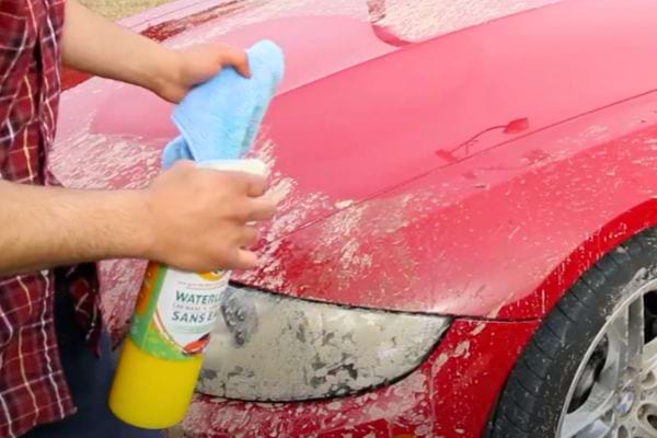 Pulvérisation d'un produit nettoyant sur la partie avant d'une voiture rouge très sale.