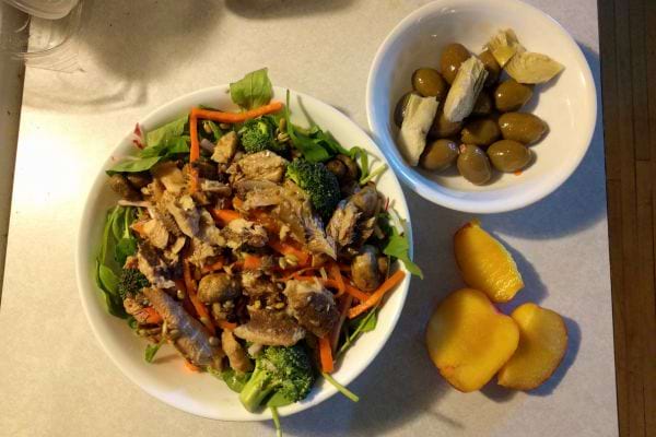 Plat avec salade riche en fibres accompagné d'olives et de morceaux de pêche.