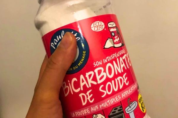 Main tenant un conteneur de bicarbonate de soude avec étiquette en français.