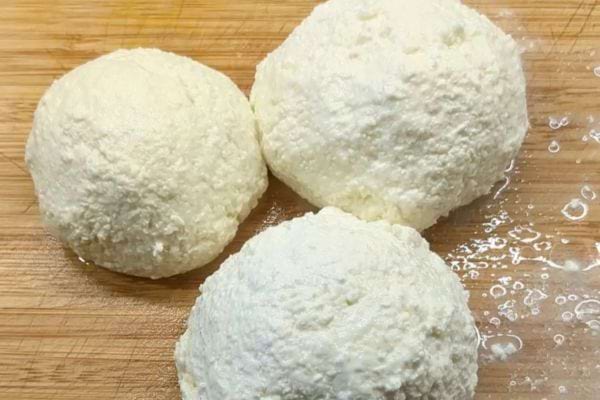 Trois boules de mozzarella fraîche sur une planche à découper en bois, avec des gouttes de liquide visible.