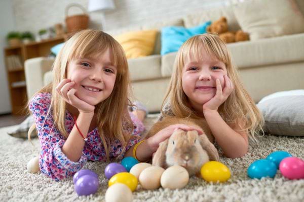 Deux filles jouant avec un lapin et des œufs de Pâques sur un tapis.