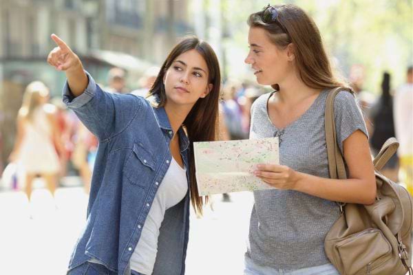 Deux femmes se repèrent dans la ville avec une carte, l'une pointant au loin.