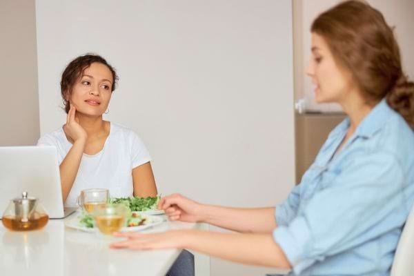 Deux femmes discutent pendant un repas, l'une écoutant attentivement l'autre.