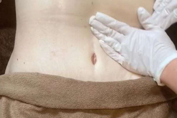 Une main gantée massant le ventre pour soulager la constipation.