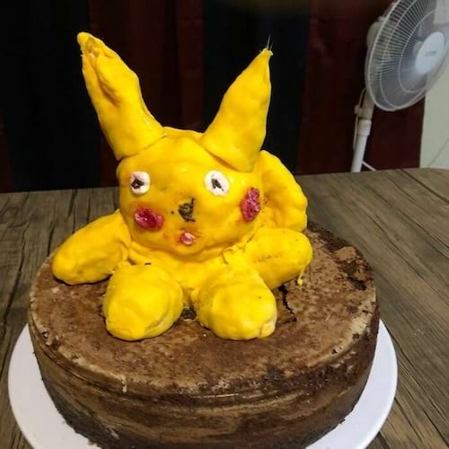 Gâteau avec une figurine de Pikachu en pâte jaune, allure déformée, visage irrégulier.