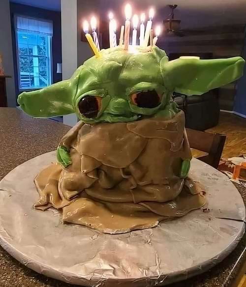 Un gâteau vert en forme de maître Yoda avec de nombreux cierges magiques.