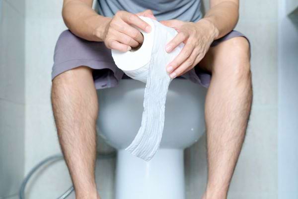 Homme assis sur un WC tenant du papier toilette.