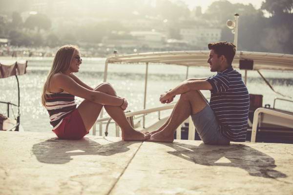 Un couple assis au bord de l'eau par une journée ensoleillée, parlant les pieds dans l'eau.
