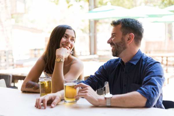 Un jeune couple riant ensemble à une table en buvant de la bière.