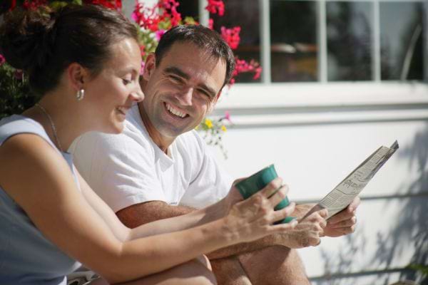 Un couple se détend à l'extérieur, lisant et riant ensemble sous un soleil éclatant.