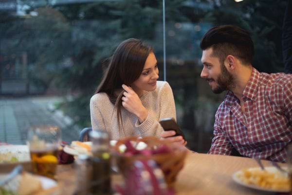 Un homme et une femme discutant à une table, un smartphone à la main.