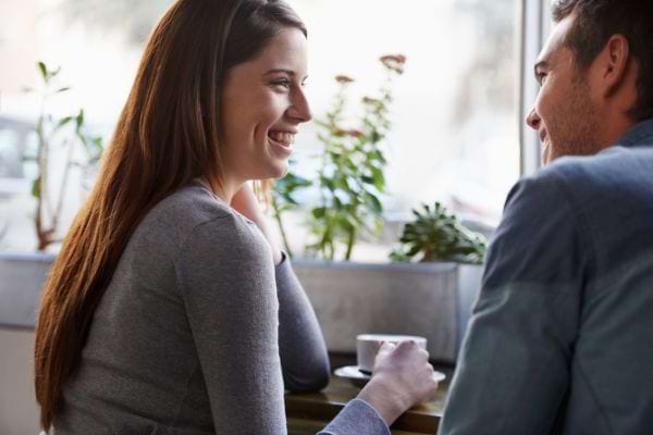 Un homme et une femme se sourient à une table de café, partageant un moment léger.