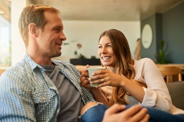 Un couple souriant confortablement installé sur un canapé, partageant des histoires autour d'une tasse de café.