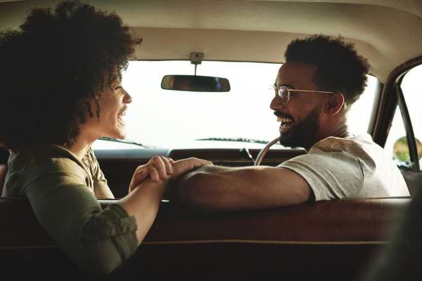 Un couple dans une voiture, riant et se tenant la main, échangeant des regards joyeux.