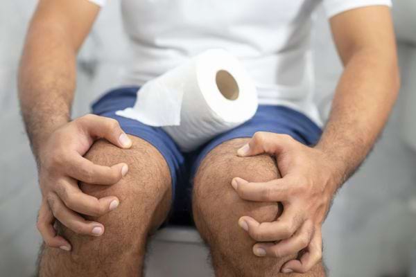 Homme assis sur un WC, tenant ses genoux, regard pensif.