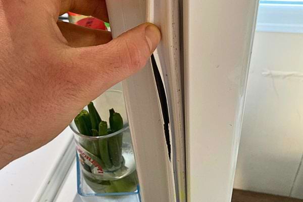 Fingerzeig auf eine beschädigte Kühlschranktürdichtung, was darauf hinweist, dass eine Reparatur erforderlich ist.