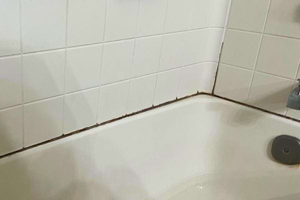 Joint de silicone noirci le long du bord d'une baignoire blanche, indiquant l'humidité.