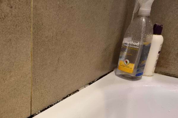 Produits de nettoyage près du joint de silicone moisi dans un coin de douche, suggérant un entretien.