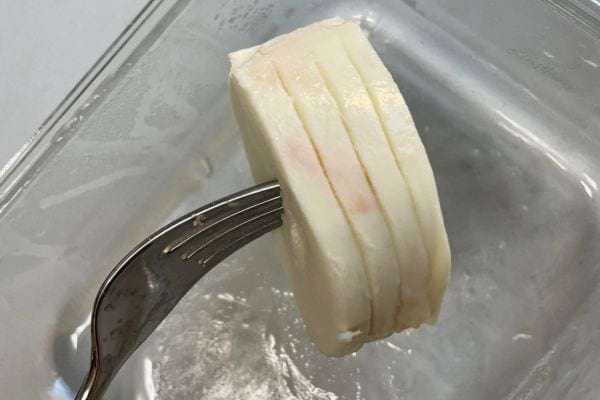 Morceau de mozzarella fraîche piqué sur une fourchette au-dessus d'un contenant en verre.