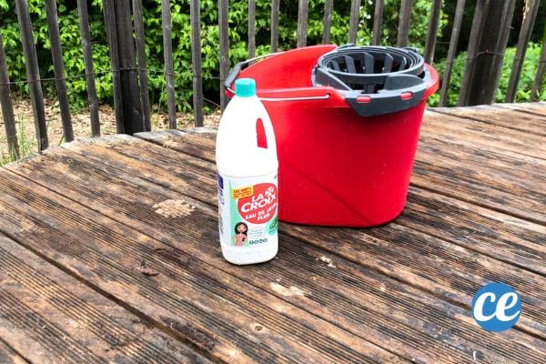 une terrasse en bois sale avec une bouteille de javel et un seau