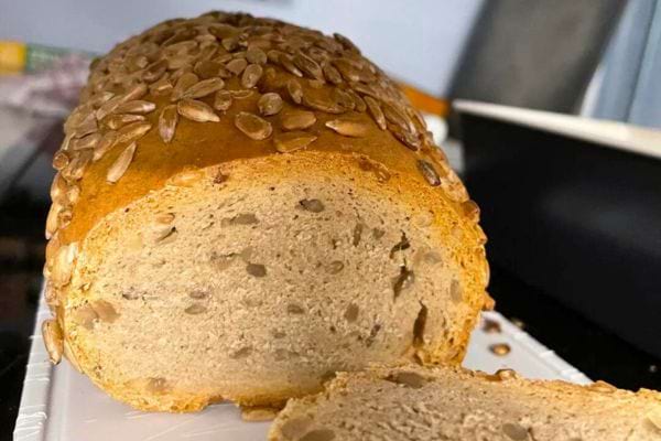 Pain oblong recouvert de graines, tranché, révélant une mie parsemée de graines, sur une assiette blanche.