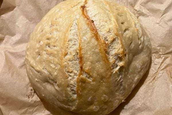 Pain rond avec une croûte dorée et des craquelures sur le dessus, cuit sur du papier sulfurisé.