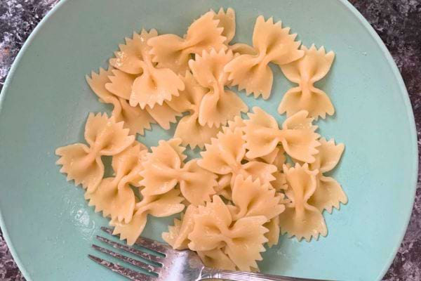 Pâtes farfalle cuites sur une assiette bleu clair avec une fourchette.
