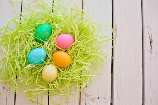 Œufs de Pâques multicolores dans un nid sur un fond de bois clair.