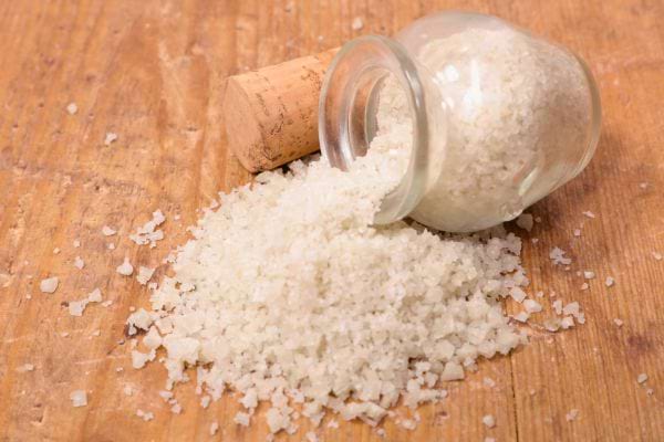 Gros sel renversé d'un récipient en verre sur une table en bois.