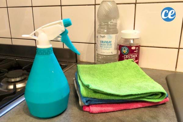 Spray bleu avec chiffons verts empilés sur un plan de travail, outils pour recette de dégraissant naturel.