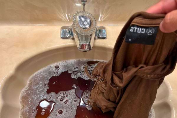 Lavage d’un t-shirt marron dans un lavabo avec de l'eau rougeâtre.