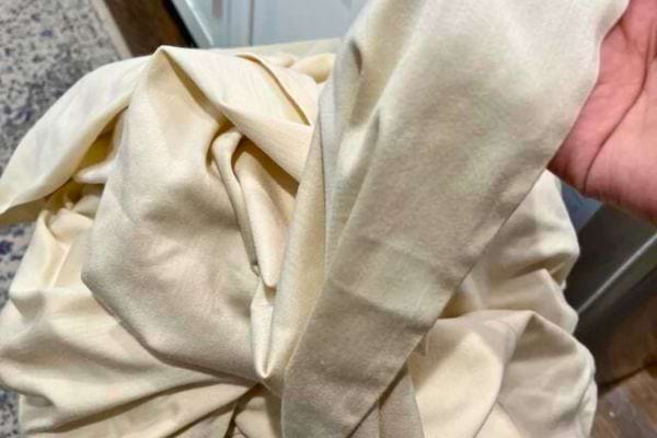 Une main tenant un tissu clair froissé.