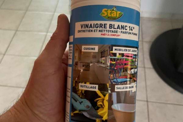 Main tenant une bouteille de vinaigre blanc.