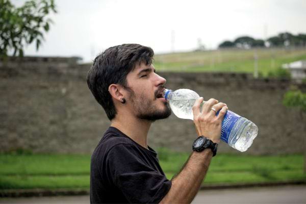 Homme en t-shirt noir boit de l'eau d'une bouteille en marchant.