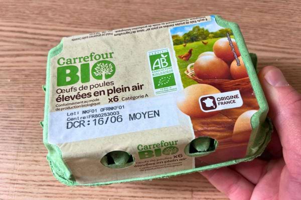 Paquet de six œufs Carrefour Bio tenu à la main, indiquant élevage en plein air et origine France.
