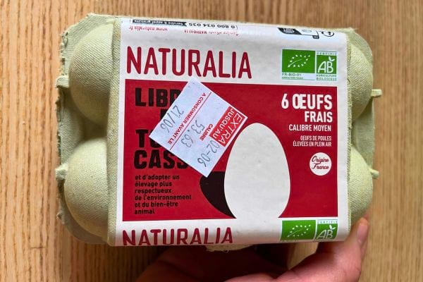 Paquet de six œufs Naturalia tenu à la main, étiqueté bio et respectueux de l'environnement.