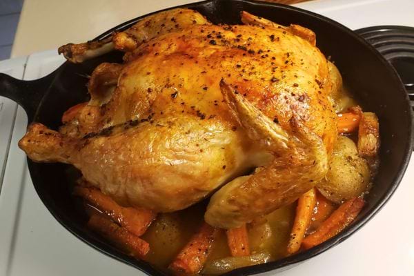 Un poulet rôti doré avec des légumes dans une poêle noire.