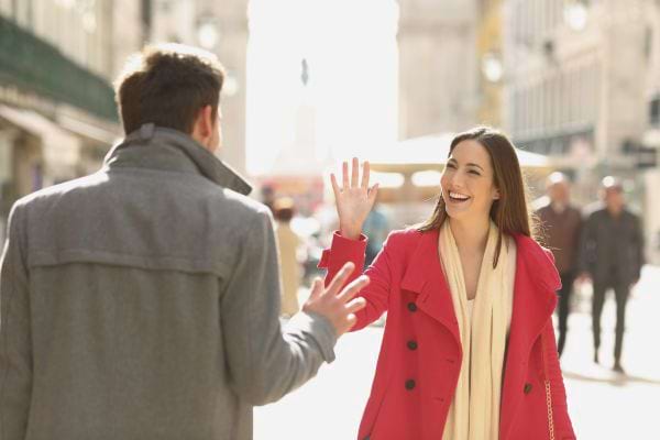 Femme en manteau rouge salue un homme sur une rue animée. 