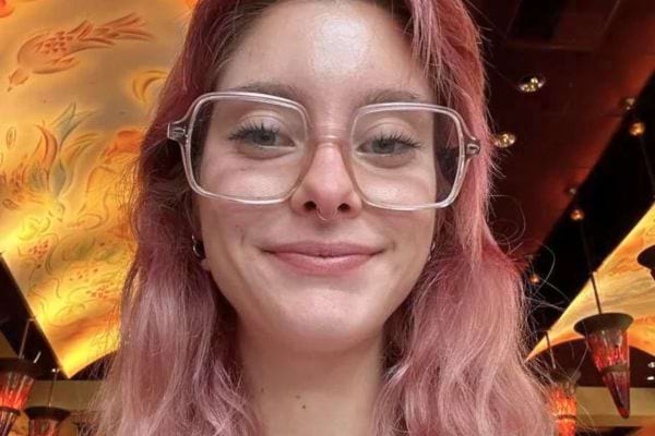 Femme souriante aux cheveux roses et lunettes.