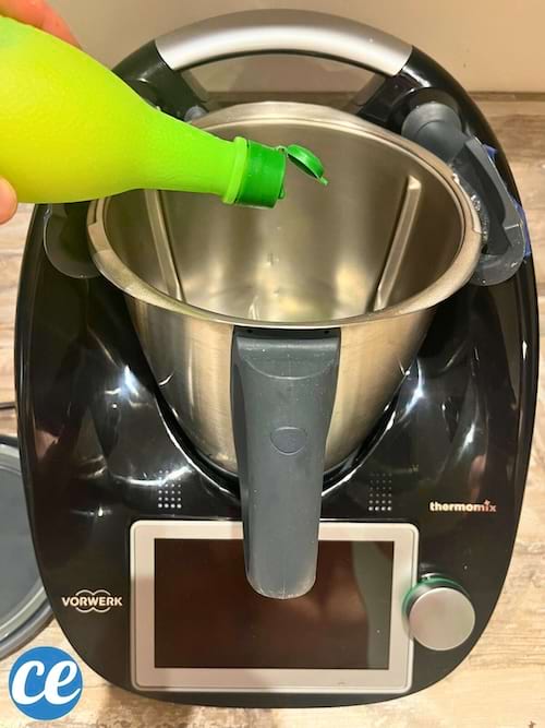 Main pressant un flacon vert, versant un liquide vert dans un Thermomix.