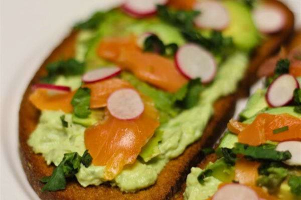 Tartine à l'avocat et saumon, garnie de radis et de fines herbes, parfaite pour un déjeuner sur le pouce.
